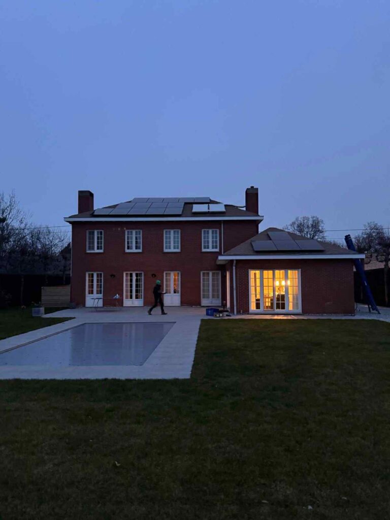 Bakstenen villa met zwarte zonnepanelen op het dak en een zwembad in de tuin, bij valavond