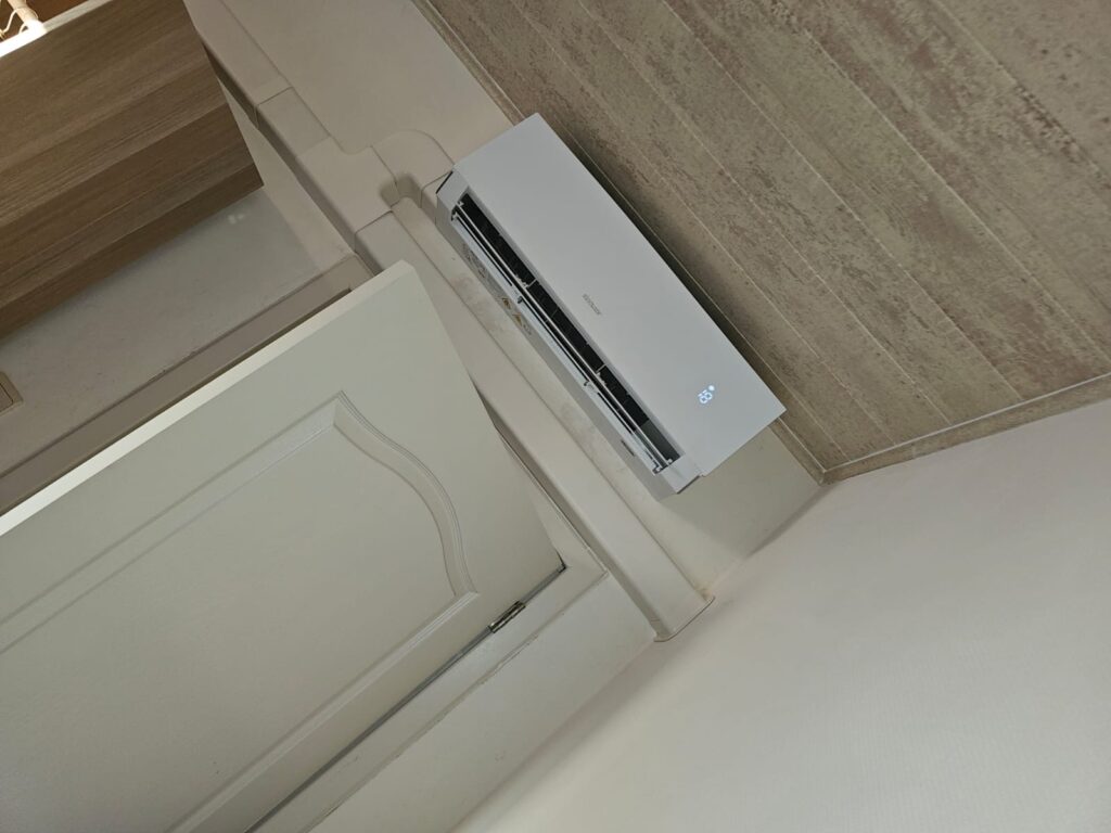 Witte airco-binnenunit hoog boven een deur, van onderen gezien