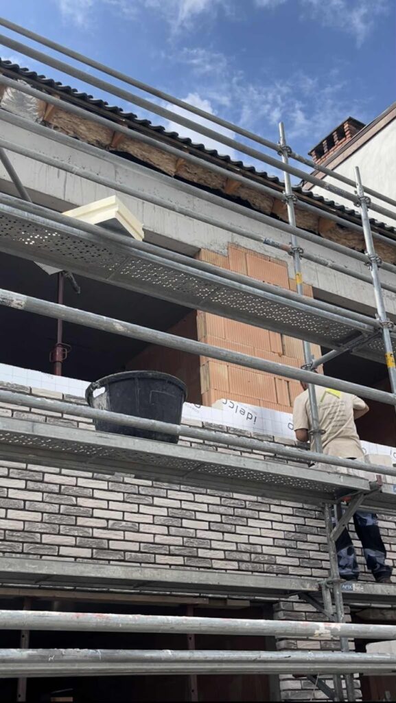 Gevel in renovatie achter de stelling, met nieuwe steenstrips half aangebracht