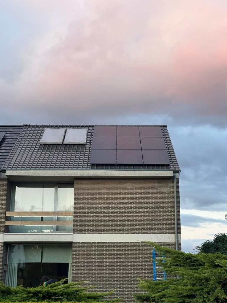 Bakstenen woning met zwarte zonnepanelen en een zonneboiler op het dak bij een roze avondlucht