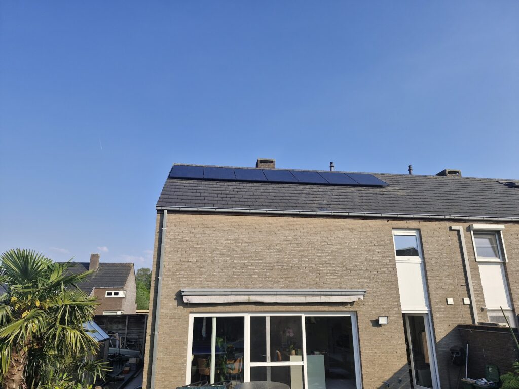 Achtergevel van een gele bakstenen woning met een rij zwarte zonnepanelen op het dak