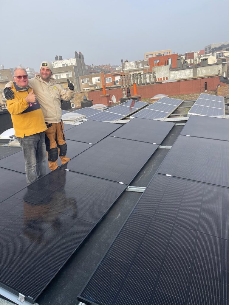 Twee installateurs lachen op een plat dak vol zwarte zonnepanelen, met de stad op de achtergrond