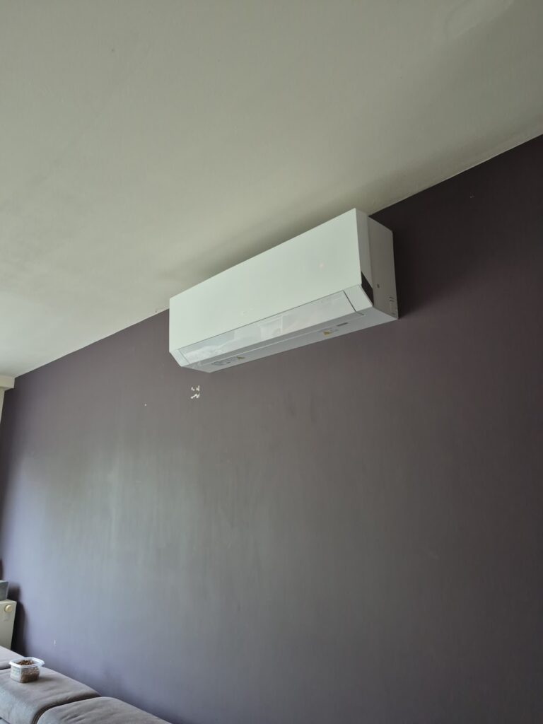 Witte airco-binnenunit hoog op een donkerpaarse muur